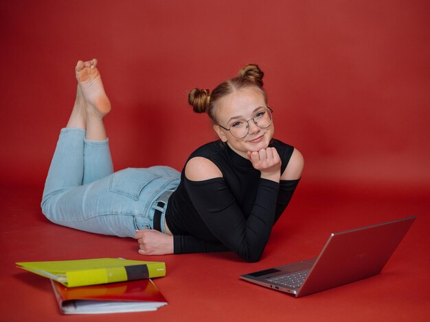 Junge Frau in einer schwarzen Bluse mit Brötchenfrisur liegt mit einem Laptop gegen einen Universitätsstudenten