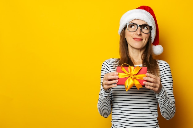 Junge Frau in einer Weihnachtsmannmütze hält ein Weihnachtsgeschenk