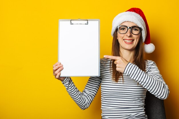 Junge Frau in einer Weihnachtsmütze hält ein Klemmbrett mit einem leeren Blatt Papier