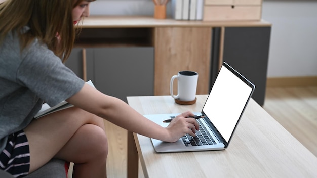 Junge Frau in Freizeitkleidung, die auf der Couch ruht und mit Laptop-Computer im Internet surft