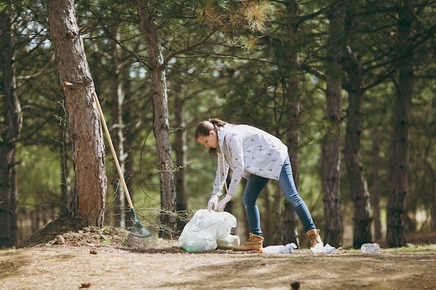 Junge Frau in Freizeitkleidung, Handschuhe, die Müll in Müllsäcke im Park oder Wald reinigen. Problem der Umweltverschmutzung