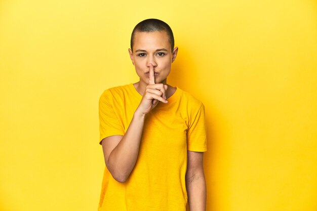 Junge Frau in gelbem T-Shirt, gelbem Studiohintergrund, der ein Geheimnis bewahrt oder um Stille bittet