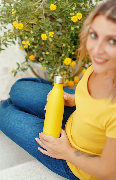 Junge Frau in gelbem T-Shirt hält eine gelbe wiederverwendbare Flasche