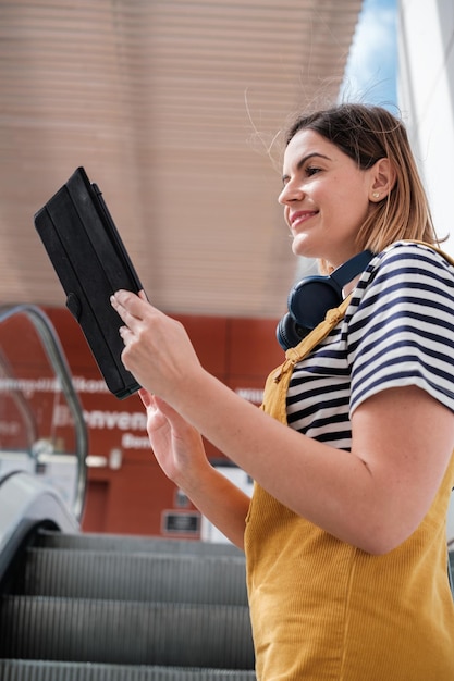 Junge Frau in gelben Latzhosen mit dem Tablet, um ihre E-Mail zu aktualisieren, während sie zur Arbeit pendelt Konzept-Lifestyle-Mode im Freien