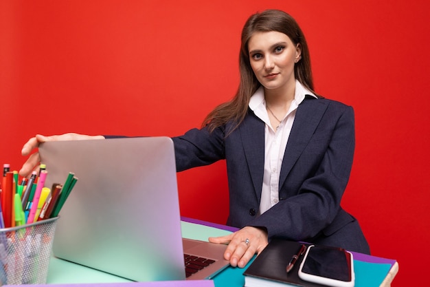 Junge Frau in Geschäftskleidung, die an einem Laptop an einer roten Wand arbeitet