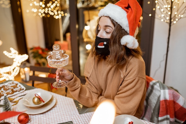 Junge Frau in Gesichtsmaske, die allein Neujahrsferien zu Hause feiert. Konzept der Quarantäne und Selbstisolation während der Epidemie an Feiertagen