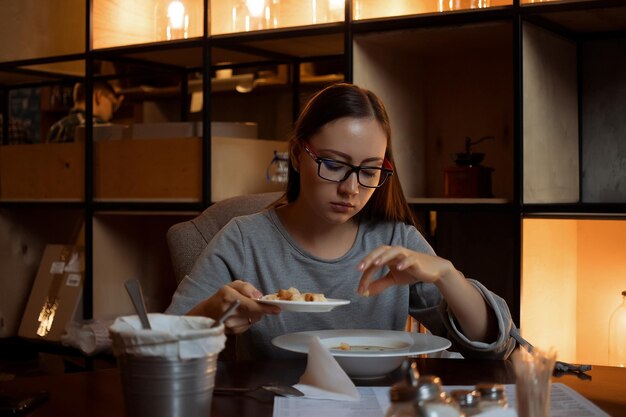 Junge Frau in Gläsern genießt leckere Suppe, während sie in einem stilvollen Restaurant am Tisch sitzt