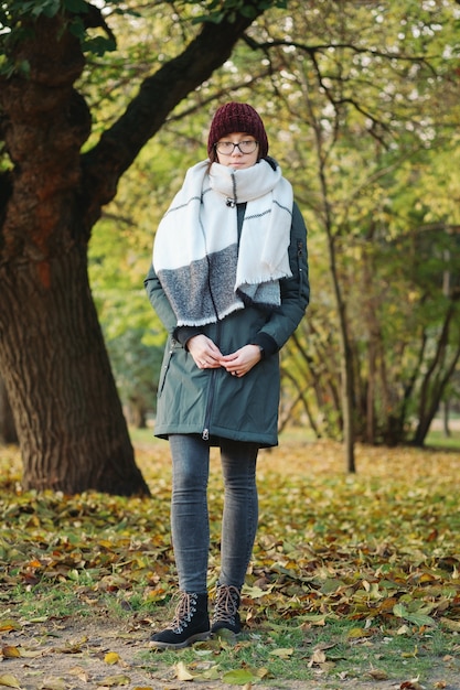 Junge Frau in Gläsern mit Schal, der im Herbstpark denkt und wartet