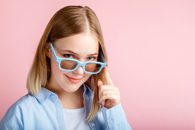 Junge Frau in Kinobrille zum Ansehen von 3D-Filmen im Kino. Lächelnder Teenager-Mädchen-Porträt-Film-Viewer in Gläsern isoliert über rosafarbenem Hintergrund mit Kopienraum.
