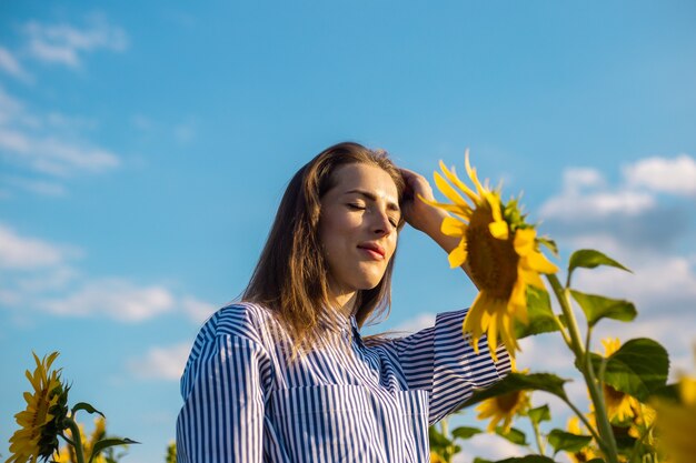 Junge Frau in Kleid und Brille bei Sonnenuntergang auf einem Sonnenblumenfeld.