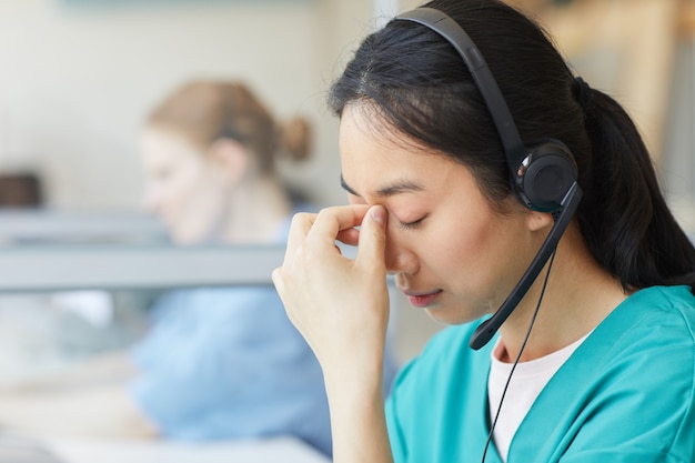 Junge Frau in Kopfhörern müde von der Arbeit hat sie Kopfschmerzen beim Sitzen am Tisch im Büro