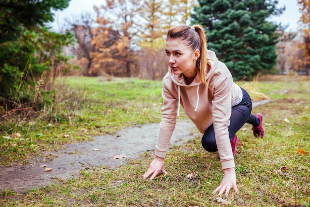 Junge Frau in Laufstartposition im Wald