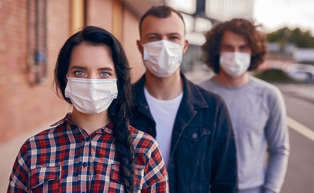 Junge Frau in medizinischer Maske, die während der Coronavirus-Epidemie in der Nähe von männlichen Freunden auf der modernen Stadtstraße steht