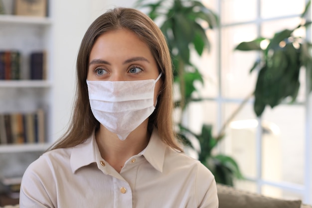 Junge Frau in medizinischer Maske zu Hause während der Epidemie.