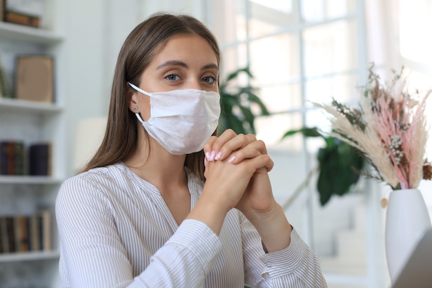 Junge Frau in medizinischer Maske zu Hause während der Epidemie.