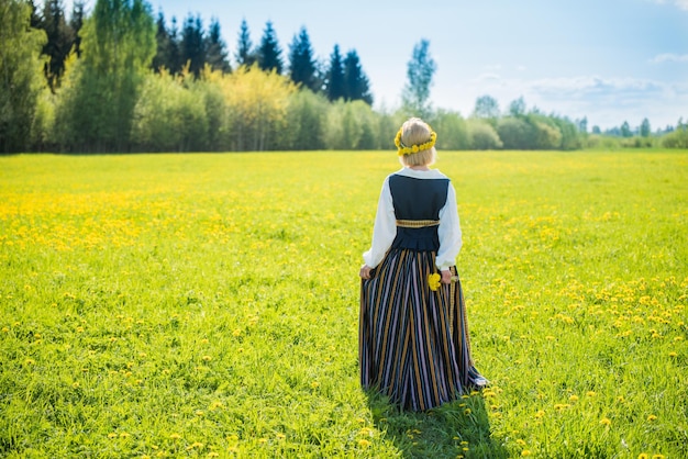 Junge Frau in nationaler Kleidung mit gelbem Löwenzahnkranz im Frühlingsfeld Frühling