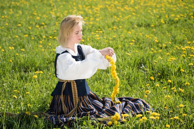 Junge Frau in nationaler Kleidung mit gelbem Löwenzahnkranz im Frühlingsfeld Frühling