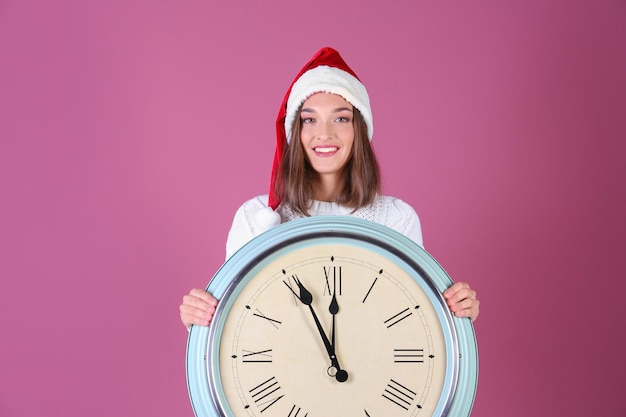 Junge Frau in Santa Hut mit Uhr auf Farbhintergrund. Weihnachts-Countdown-Konzept