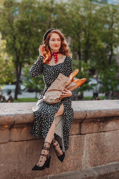 Junge Frau in schwarzem Kleid, die ein Papierpaket mit französischen Baguettes hält Lebensmittelfoto einer Brotbäckerei