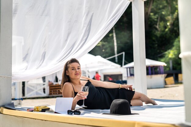 Junge Frau in schwarzem Kleid verbringt die Sommerzeit und entspannt sich in einem Himmelbett in der Nähe des Strandes