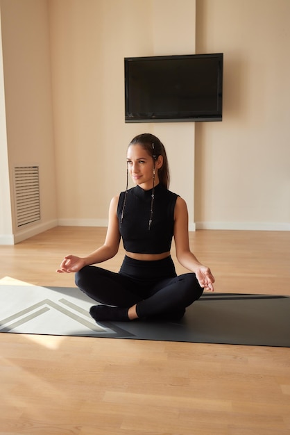 Junge Frau in schwarzem Sportanzug, die drinnen Yoga-Pose ausübt