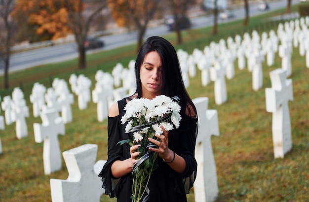 Junge Frau in schwarzer Kleidung, die den Friedhof mit vielen weißen Kreuzen besucht Konzeption von Beerdigung und Tod