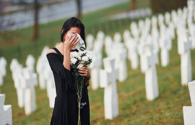 Junge Frau in schwarzer Kleidung, die den Friedhof mit vielen weißen Kreuzen besucht Konzeption von Beerdigung und Tod