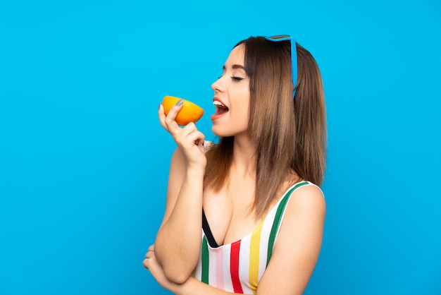 Junge Frau in Sommerferien über dem Blau, das eine Orange hält