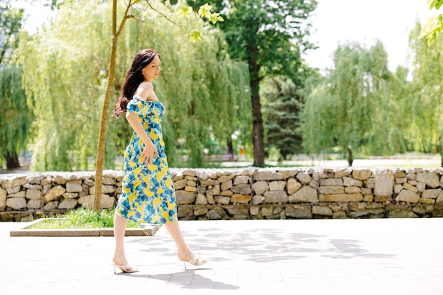 Junge Frau in Sommerkleidung geht im grünen Park und genießt die Sonne Spielhaftes und schönes Mädchen an einem warmen sonnigen Tag