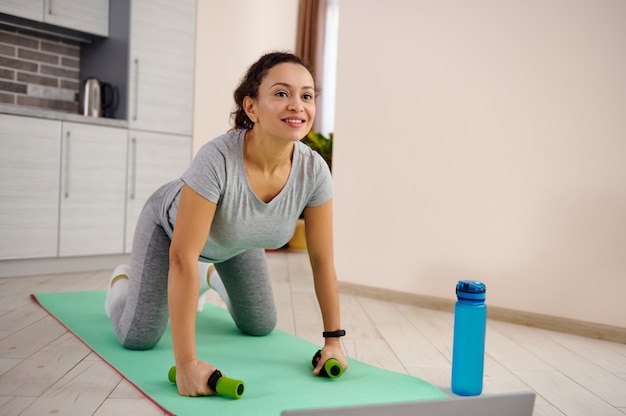 Junge Frau in Sportbekleidung, die auf einer Fitnessmatte während eines Tages zu Hause ausübt