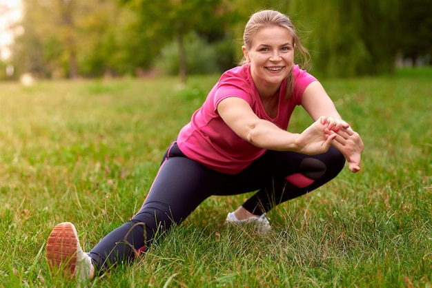 Junge Frau in Sportbekleidung macht Ausfallschritte und streckt sich im Park Fitnesstraining im Freien