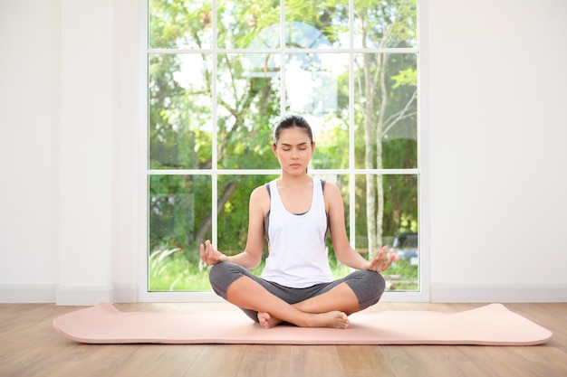 Junge Frau in Sportbekleidung macht Meditationsübungen und Yoga im Innenbereich