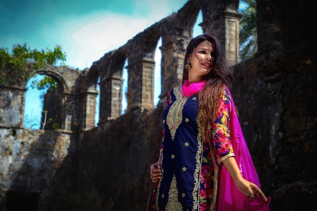 Junge Frau in traditioneller Kleidung steht an einer alten Mauer