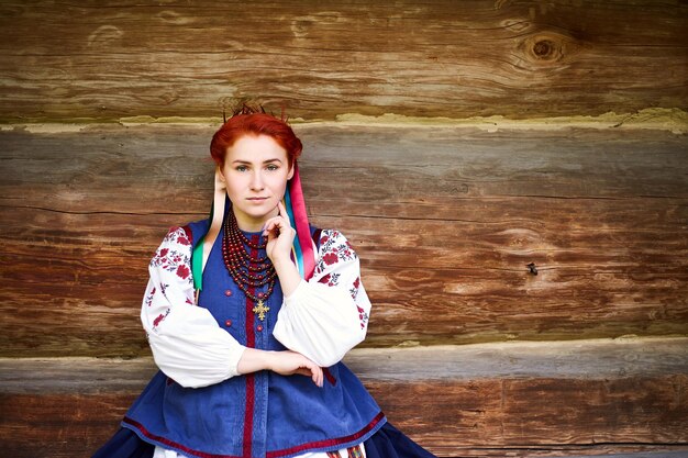 Foto junge frau in ukrainischer nationaltracht lächelnde junge dame in traditioneller kleidung in der nähe des alten holzhauses frieden in der ukraine