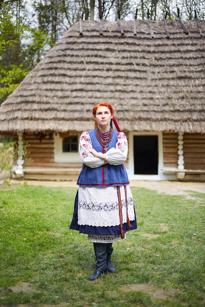 Junge Frau in ukrainischer Nationaltracht Lächelnde junge Dame in traditioneller Kleidung in der Nähe des alten Holzhauses Frieden in der Ukraine