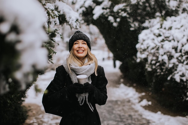 Junge Frau in warmer Kleidung genießt im Schnee eine Kaffeetasse zum Mitnehmen