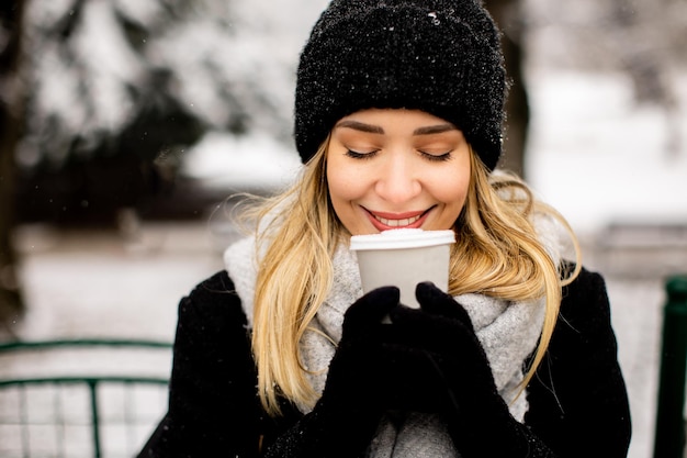 Junge Frau in warmer Kleidung genießt im Schnee eine Kaffeetasse zum Mitnehmen