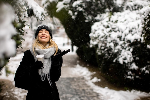 Junge Frau in warmer Kleidung genießt im Schnee eine Kaffeetasse zum Mitnehmen