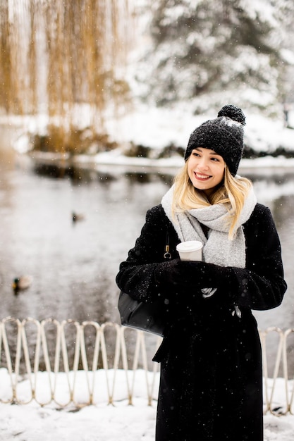 Junge Frau in warmer Kleidung genießt im Schnee eine Kaffeetasse zum Mitnehmen