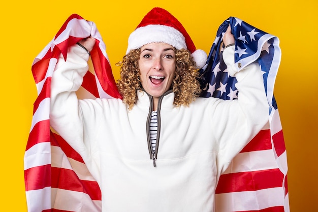 Junge Frau in Weihnachtsmannmütze schreit freudig mit der usa-Flagge auf gelbem Hintergrund