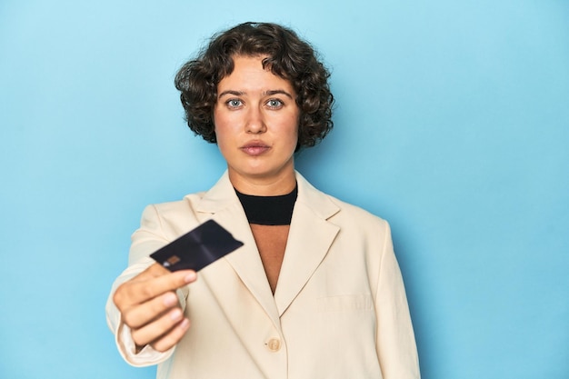 Junge Frau in weißem Anzug und Blazer hält eine Kreditkarten-Studioaufnahme