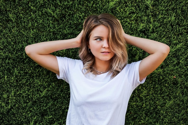 Junge Frau in weißem Hemd mit natürlichem Make-up, die an einer grünen Hecke steht