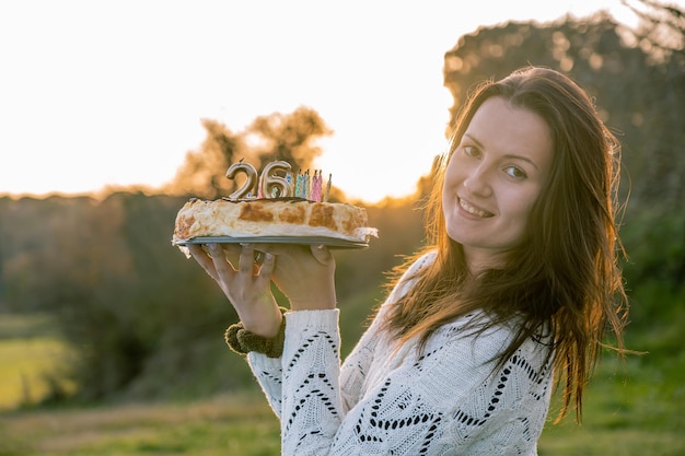 Junge Frau in weißem Pullover hält einen Geburtstagskuchen mit fehlgelegten Kerzen