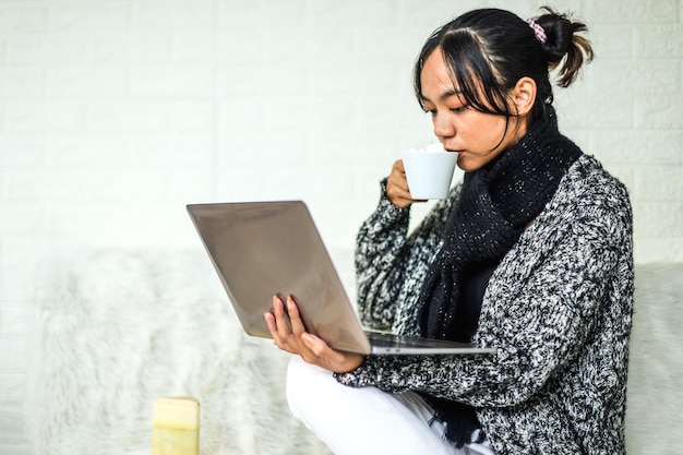 Junge Frau in Winterkleidung, die Online-Shops auf Cyber-Monday-Verkäufe am Laptop überprüft, während sie genießt