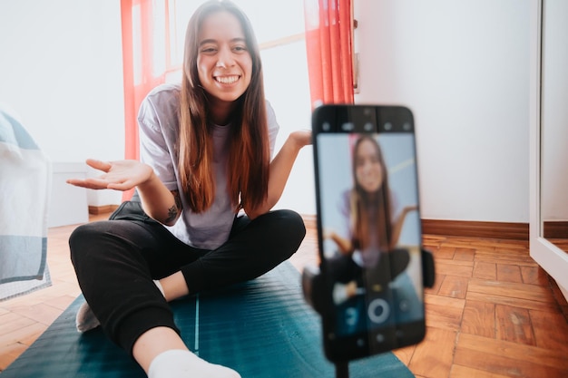 Junge Frau Infuencer erklärt Anhängern vor dem Smartphone Yoga-Positionen beim Erstellen von Inhalten für soziale Medien