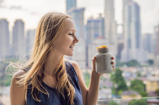 Junge Frau isst Chia-Pudding auf ihrem Balkon mit Blick auf die Großstadt