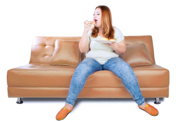 Foto junge frau isst donuts, während sie auf dem sofa sitzt