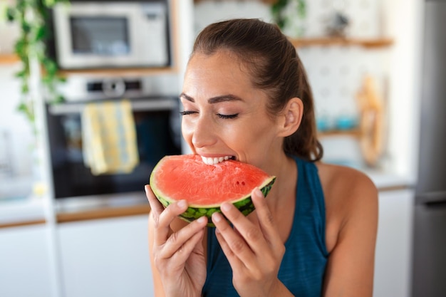 Junge Frau isst ein Stück Wassermelone in der Küche Porträt der jungen Frau, die eine Wassermelone genießt