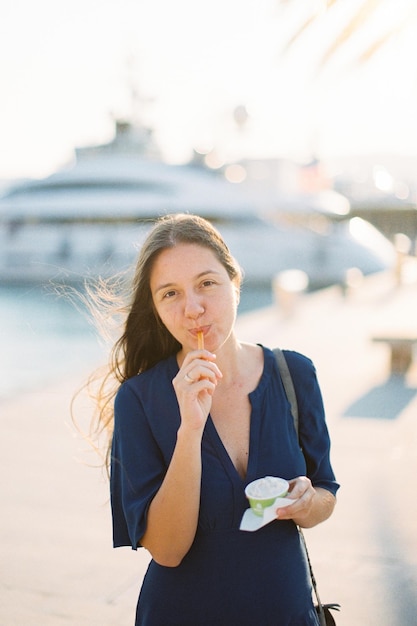 Junge Frau isst Eis mit einem Löffel aus einer Tasse auf dem Pier
