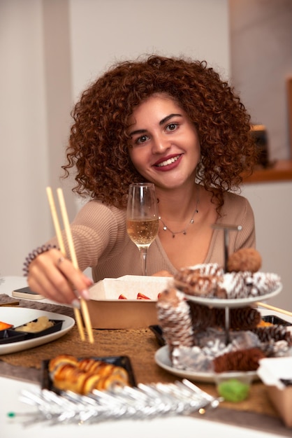 Junge Frau isst Sushi asiatisches Essen und Nudeln mit Stäbchen aus der Lieferung zum Mitnehmen